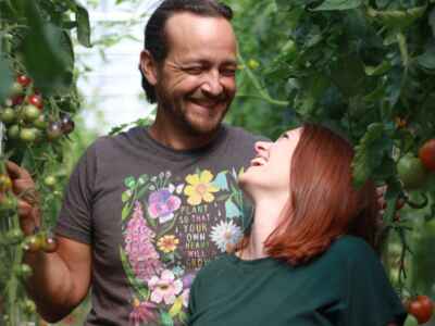 A man and a woman stand side by side amongst tomatoes.